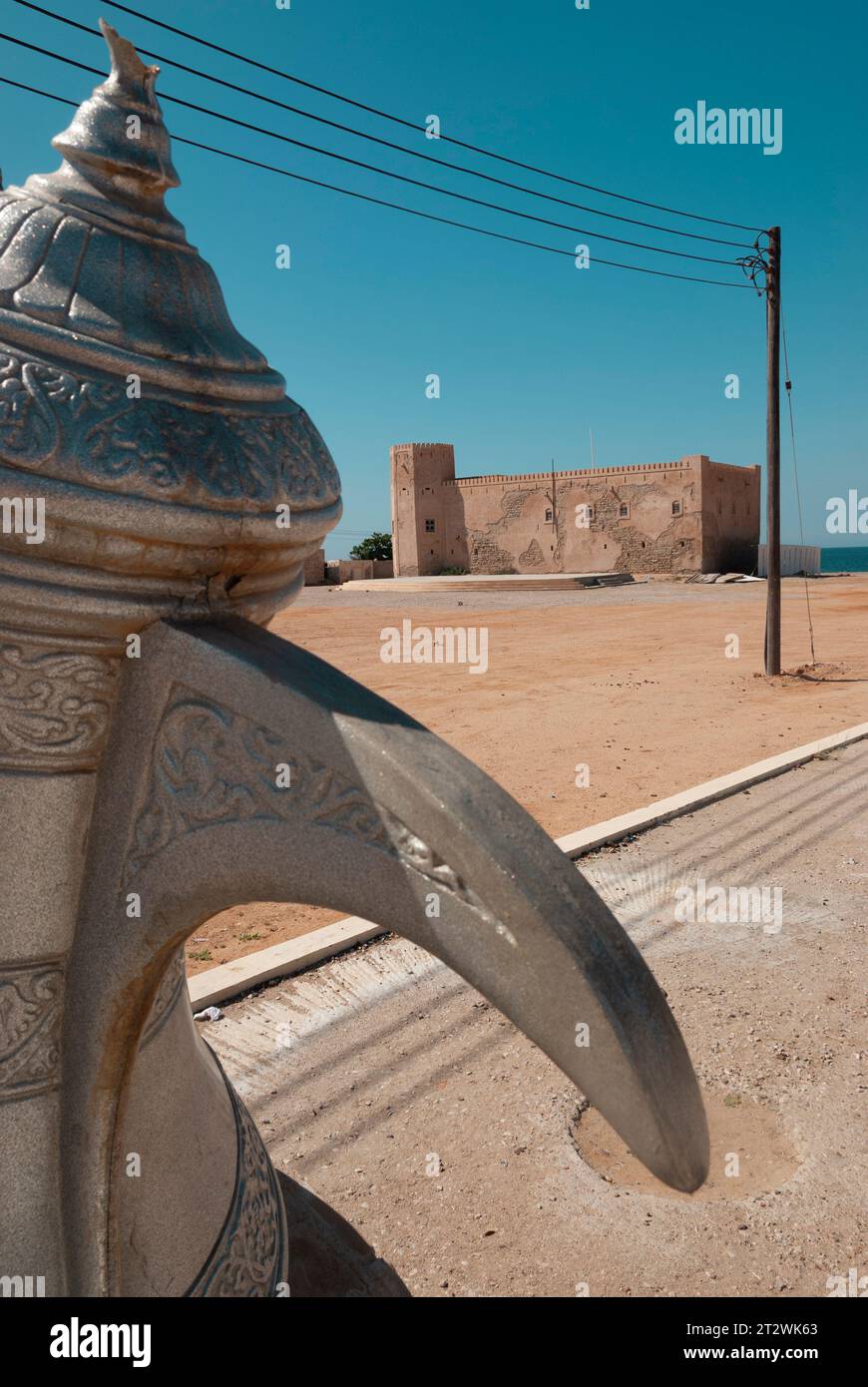 Der Auslauf einer Kanne mit dem alten Schloss Mirbat im Hintergrund in Mirbat in Oman Stockfoto