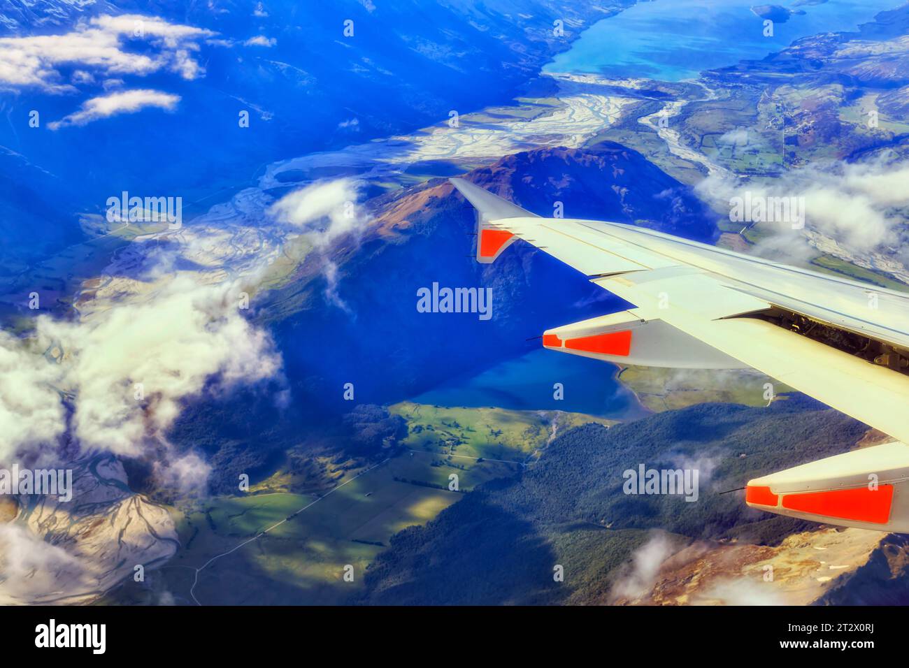 Flugzeugflügel mit Triebwerken, die über Berggipfel und Gebirgszüge der Südinsel Neuseelands über landwirtschaftliche Farmen und Seen fliegen. Stockfoto