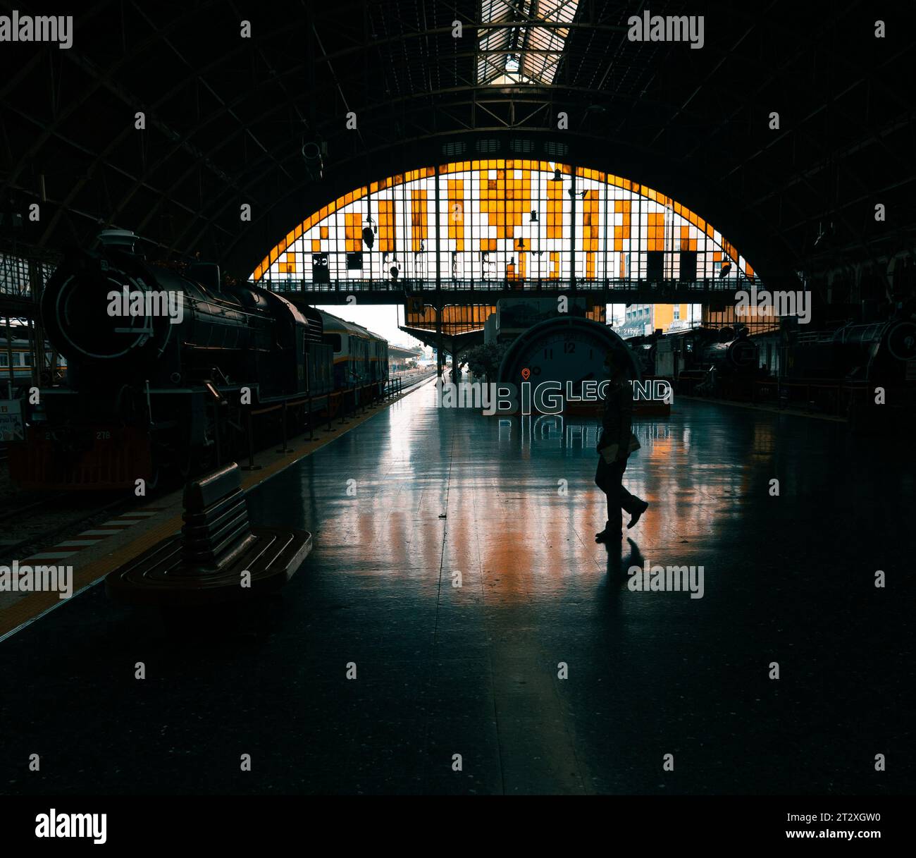 Mann, der auf einem Bahnsteig zu einer alten Dampfeisenbahn läuft. Im Vordergrund befindet sich ein Sitzplatz und im Hintergrund ein Buntglasfenster. Stockfoto