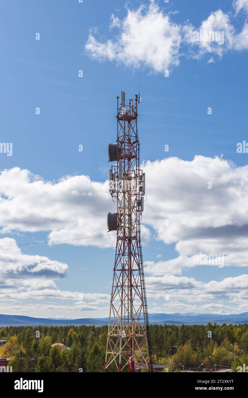 Telekommunikationsturm mit verschiedenen Antennen vor dem Hintergrund eines blauen bewölkten Himmels und Bergen in der Ferne Stockfoto