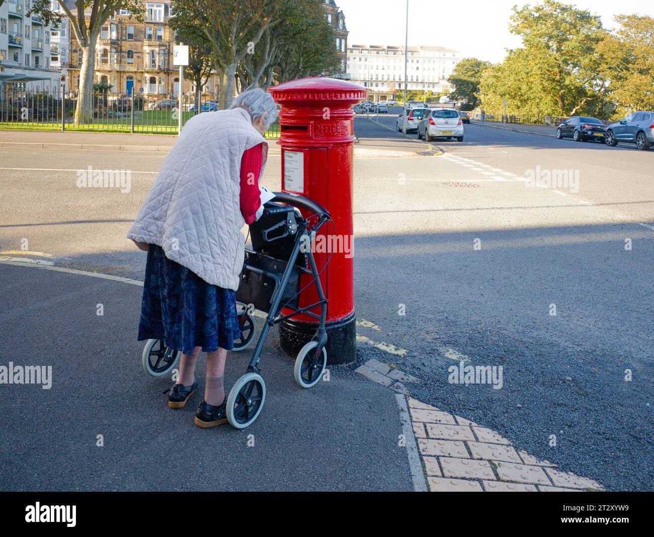 Eine ältere Frau mit Gehhilfe, die Briefe in einen viktorianischen Briefkasten in Scarborough postet Stockfoto
