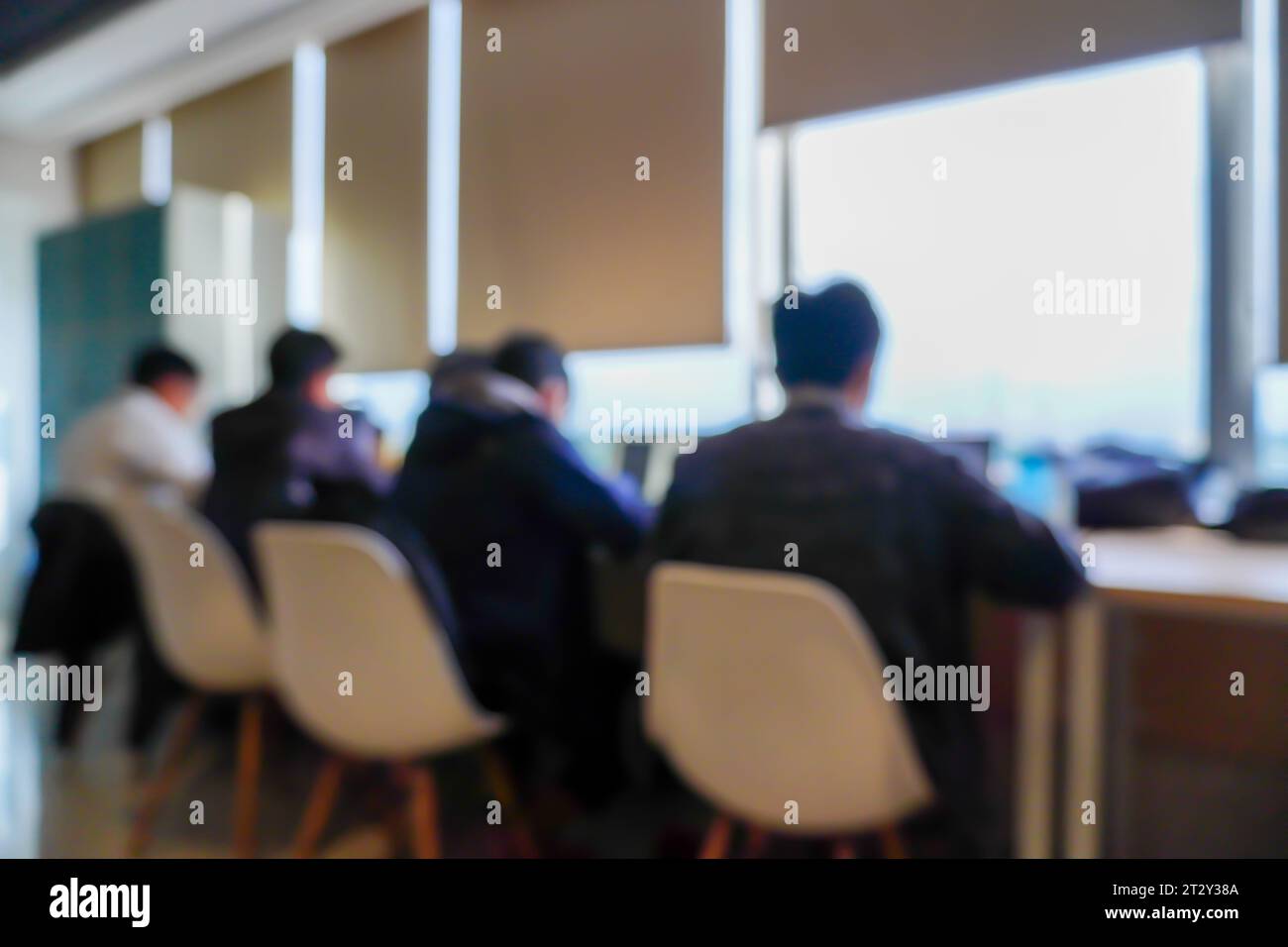 Eine fesselnde Gruppe von Männern, die fleißig vor ihren Laptops sitzen und arbeiten, in einem Raum in der Nähe eines Fensters Stockfoto