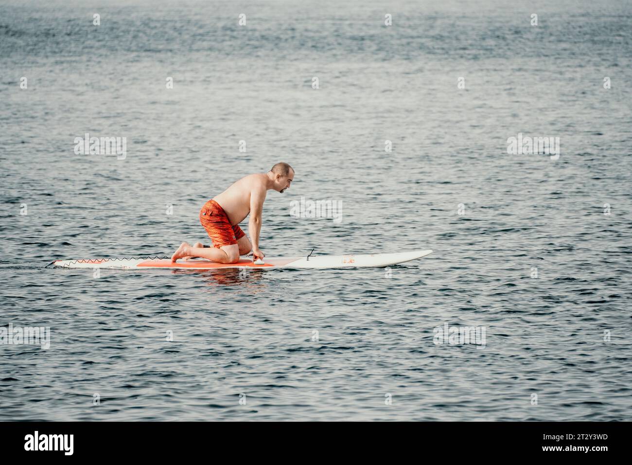 Aktiver reifer männlicher Paddler mit seinem Paddleboard und paddeln im Sommer auf dem Meer. Ein glücklicher Seniorenmann steht mit einem SUP-Brett. Stand-Up-Paddle-Boarding - Stockfoto