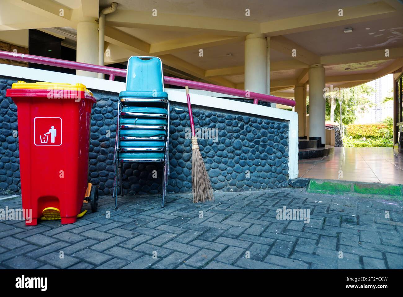 Naturbesen, rote Abfallbehälter aus Kunststoff im Freien und gestapelte Stühle im Hof des Hauses Stockfoto
