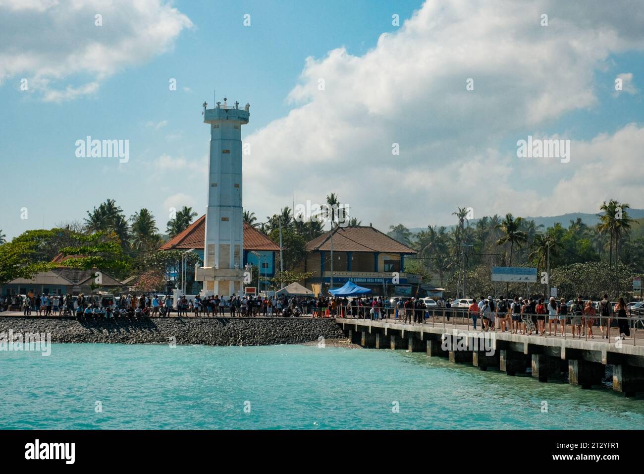 Erkunden Sie die lebhafte Atmosphäre des Hafens Nusa Penida, wo türkisfarbenes Wasser auf einen belebten Pier trifft, der vor Aktivität strotzt. Gegen die Leinwand eines Brillianers Stockfoto