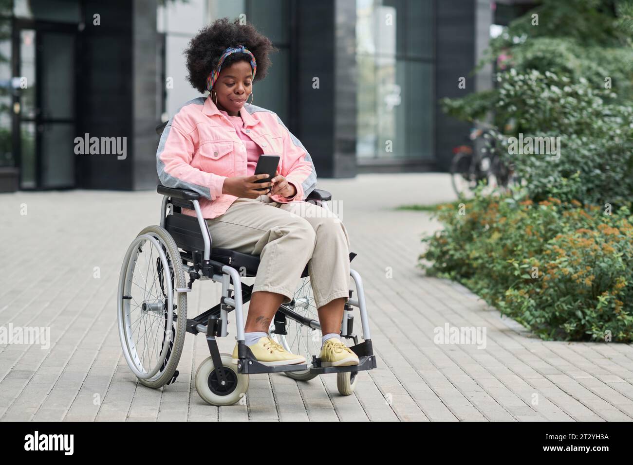 Afroamerikanische Frau mit Behinderung, die im Rollstuhl sitzt und im Freien ein Smartphone benutzt Stockfoto