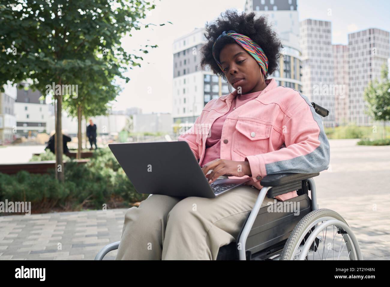 Afroamerikanerin sitzt im Rollstuhl in der Stadt und benutzt einen Laptop Stockfoto