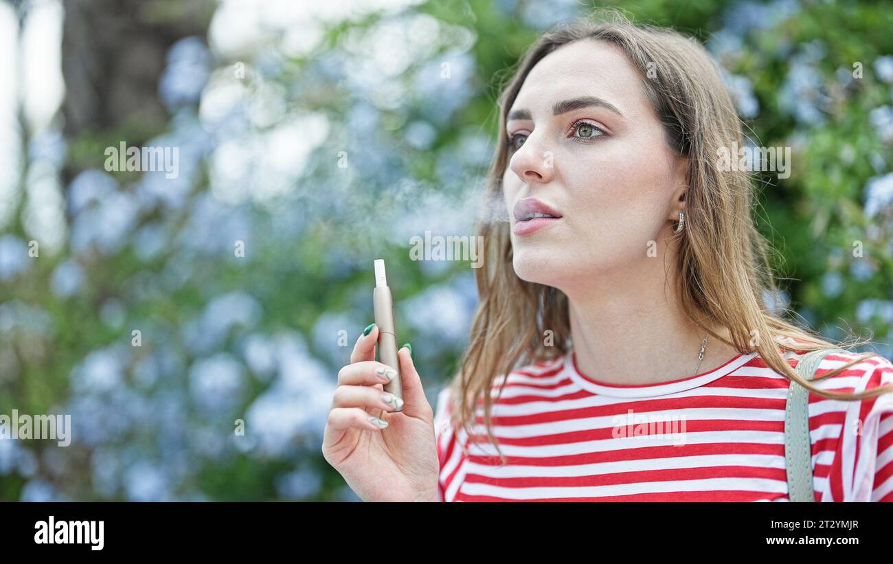 Junge blonde Frau, die Vaper im Park raucht Stockfoto