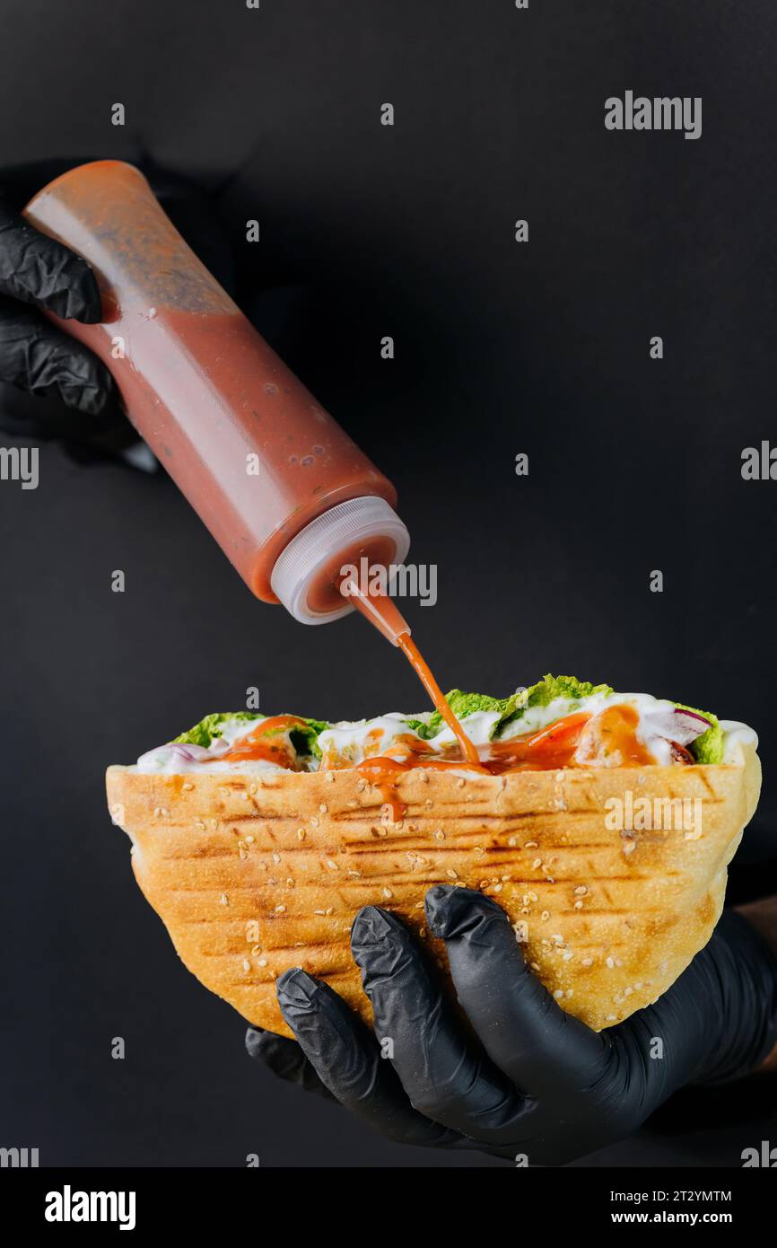 Kocht mit der Hand Soße in Döner-Döner durch gerissene Löcher auf schwarzem Papierhintergrund Stockfoto