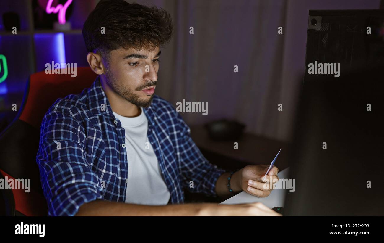 Ein aufregender Nachtstream, junger arabischer Mann spielt virtuell mit Computer und Kreditkarte im Spielzimmer Stockfoto