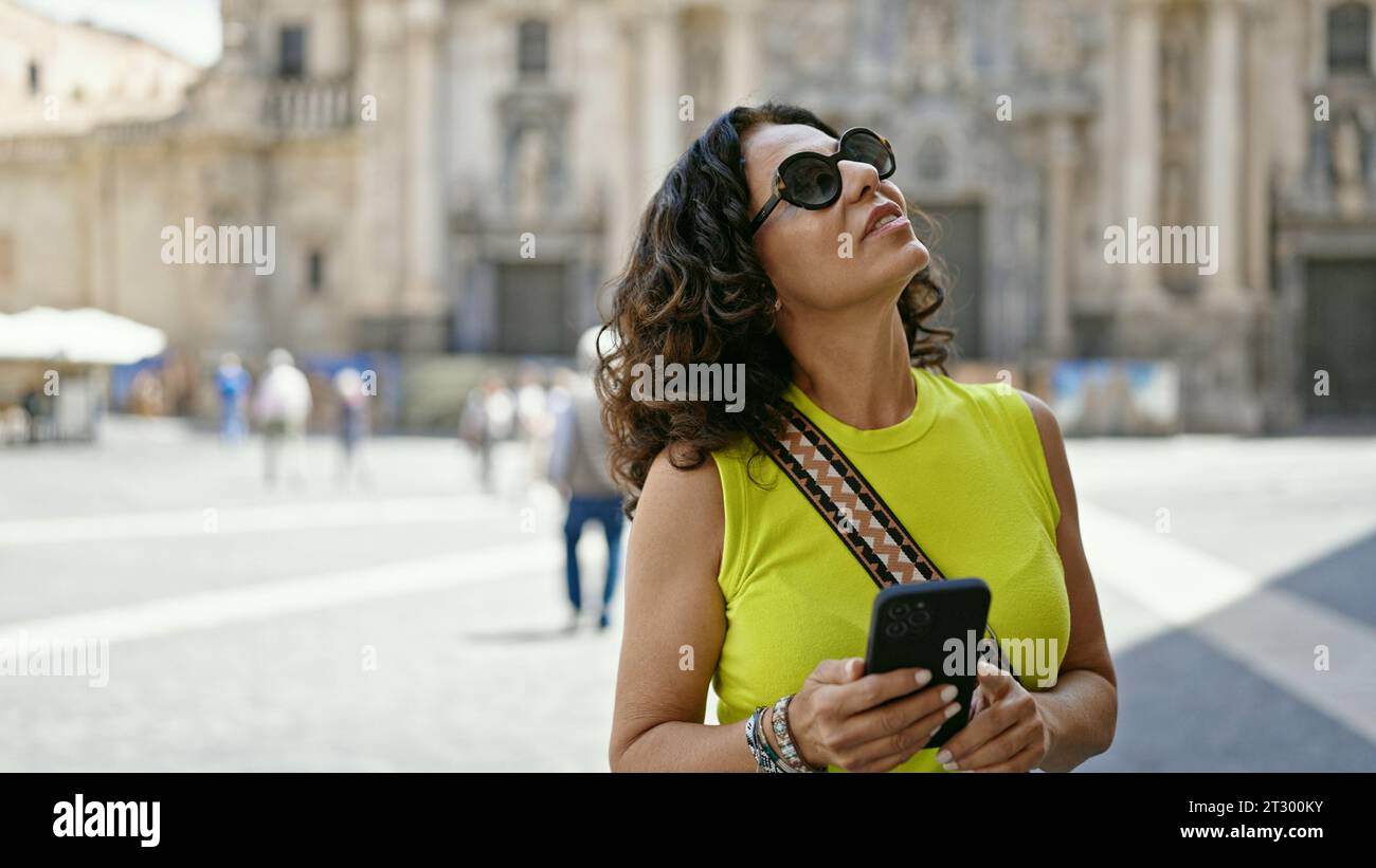 Mittelalter hispanische Frau, die ein Smartphone auf der Straße benutzt Stockfoto