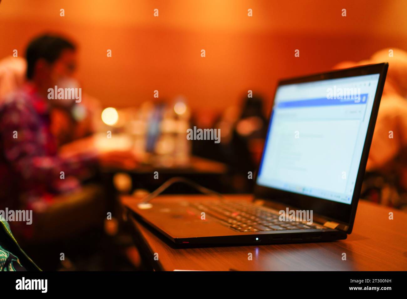 Auf dem Tisch steht ein unscharfer Laptop mit einem unscharfen Hintergrund eines Mannes, der bei einer Seminarsitzung arbeitet Stockfoto