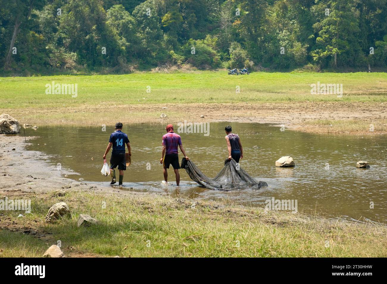 Tauchen Sie ein in die uralte Tradition, während drei Männer geschickt Netzfischen am ruhigen Ufer des Patenggang Lake betreiben. Diese Szene erfasst Stockfoto