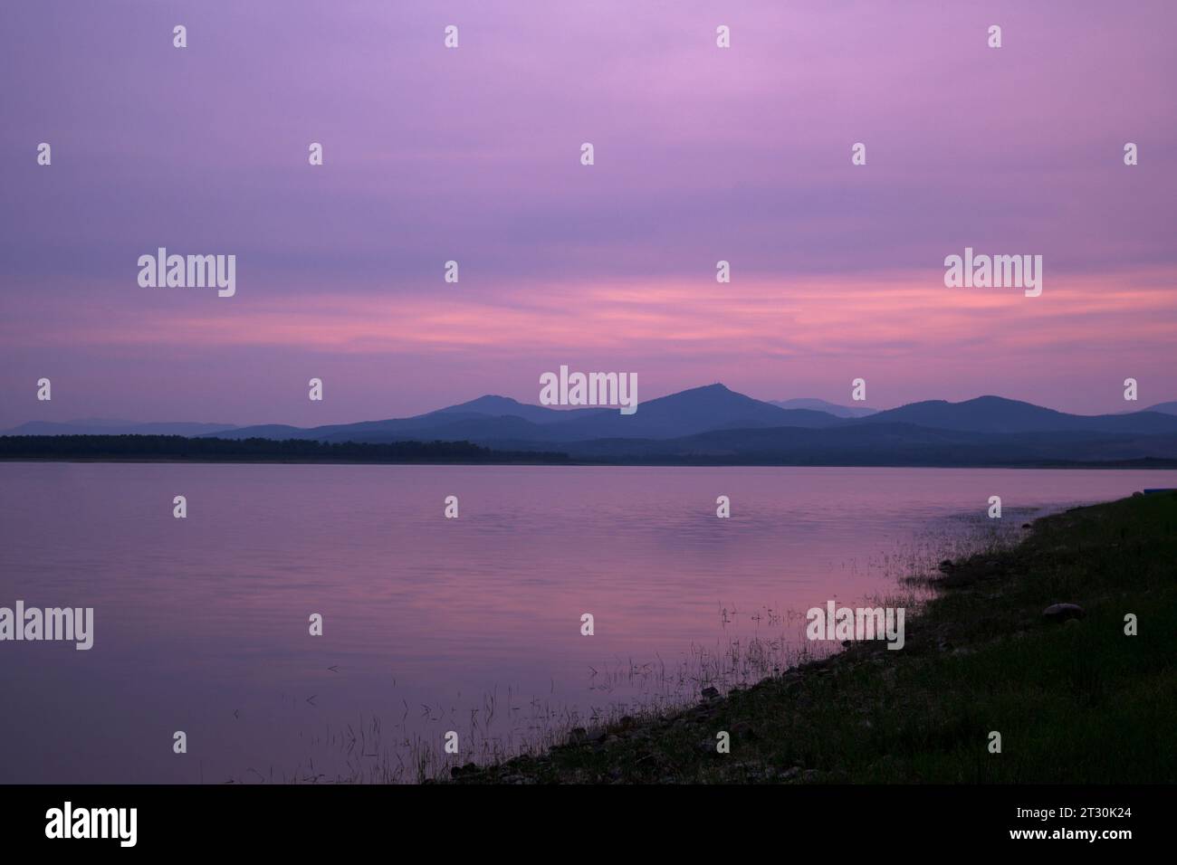 Sonnenuntergang mit goldenem magentarotem Himmel mit Bergen im Hintergrund und Reflexion im Wasser Stockfoto