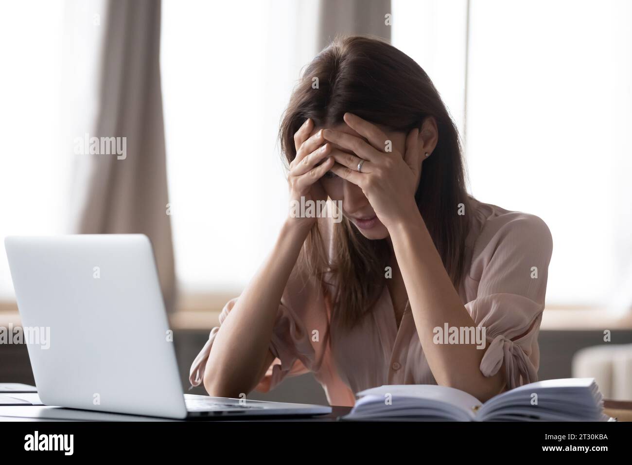 Frau, die am Schreibtisch sitzt und den Kopf mit den Händen hält, fühlt sich gestresst Stockfoto
