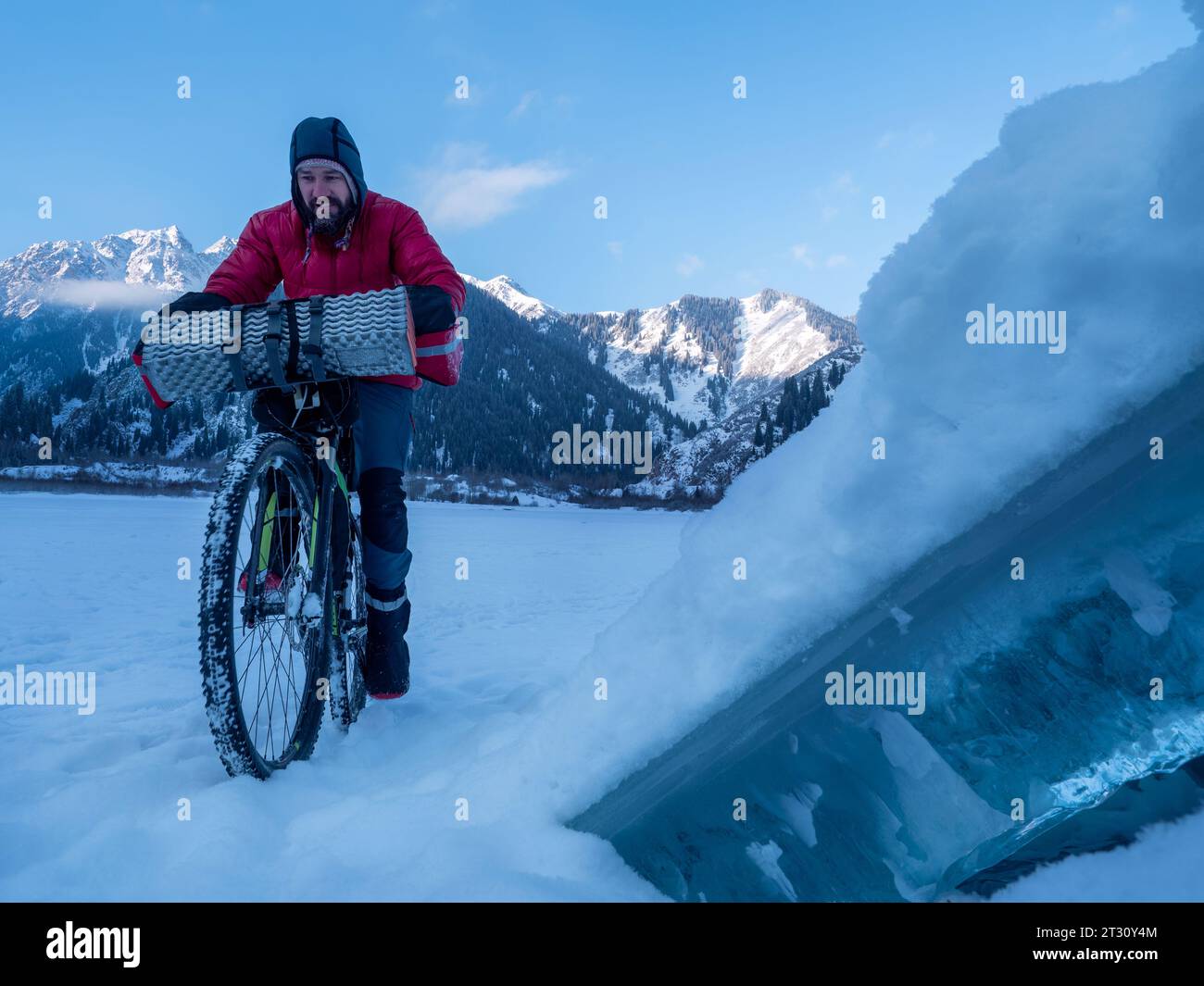 Im Winter fährt ein Mann mit dem Fahrrad in den Bergen. Radtour im Winter. Schlittschuhlaufen auf dem Eis eines gefrorenen Bergsees. Früher Wintermorgen hoch im Stockfoto