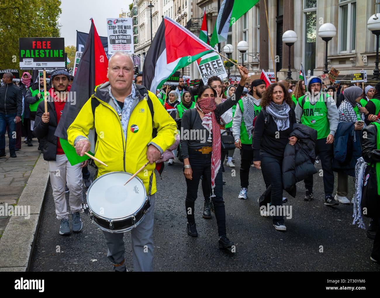 London / UK - 21. Oktober 2023: Ein pro-palästinensischer Demonstrant spielt Trommeln, während er mit anderen Menschen marschiert, die Plakate und Fahnen halten, bei einer großen Demonstration Stockfoto