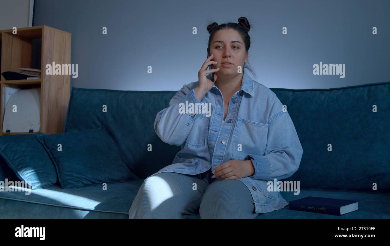 Eine Frau, die Haushaltsarbeiten erledigt. Medien. Eine wunderschöne Frau in Jeans mit wunderschöner Frisur, die auf der Couch sitzt und ein Tagebuch und ein Telefon hat. Stockfoto