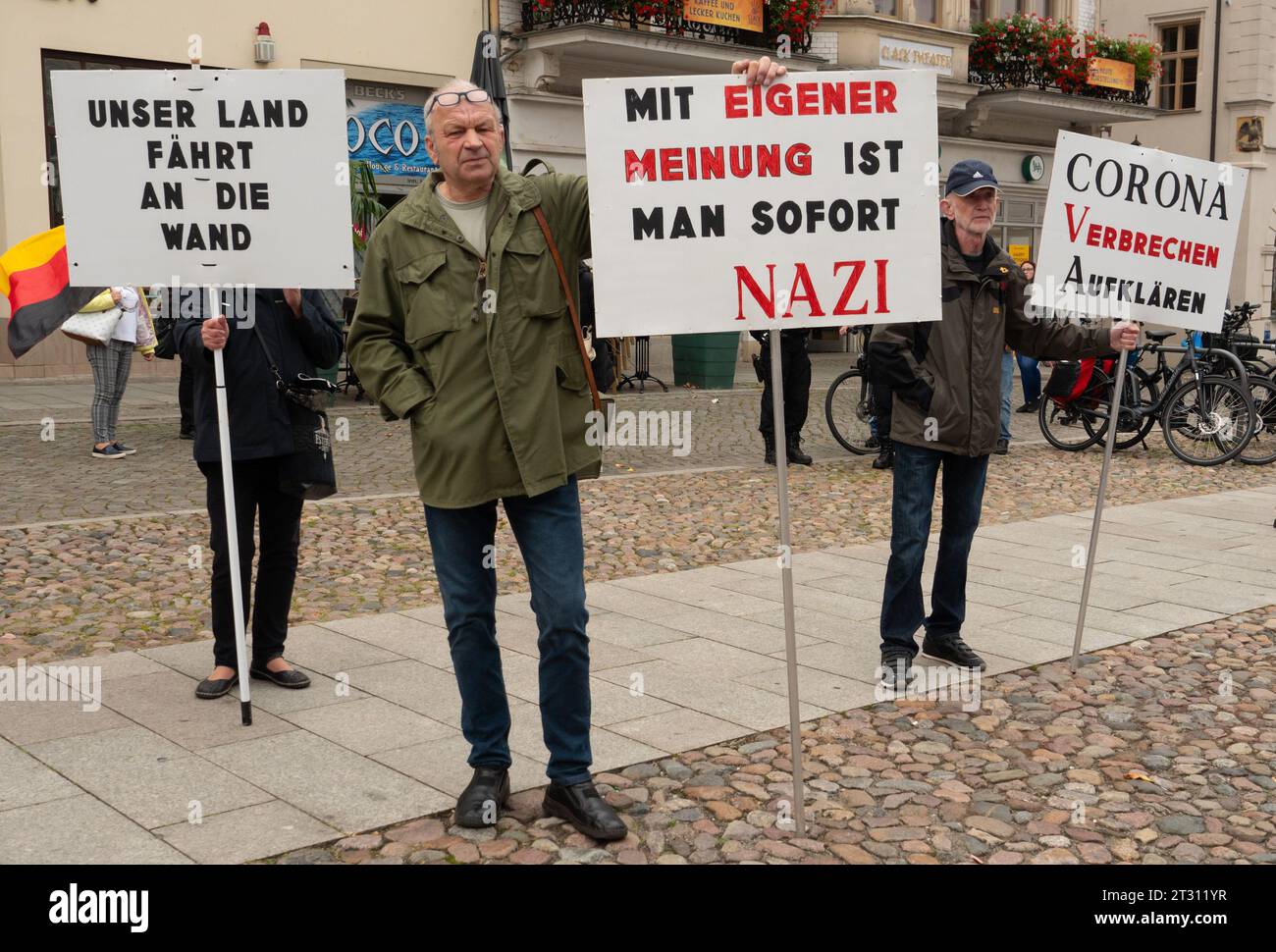 07. Oktober 2023, Sachsen-Anhalt, Lutherstadt Wittenberg: ACHTUNG: Nur im Vollformat verwenden. 07.10.2023, Lutherstadt Wittenberg. Menschen demonstrieren gegen die Corona-Politik der deutschen Regierung und gegen die Position der Regierung im Ukraine-Krieg. Sie verlangten "Frieden mit Russland" und eine Neubewertung dessen, was sie "Corona-Verbrechen" nennen. Ein Mann hält ein Schild mit der Aufschrift „mit deiner eigenen Meinung bist du sofort ein Nazi“ (auf der abgewendeten Rückseite seines Schildes steht „Wir haben eine Politik zwischen Größenwahn und Ohnmacht“). Ein zweiter Mann (r) hält ein Schild mit der Aufschrift "Löse Corona CR Stockfoto