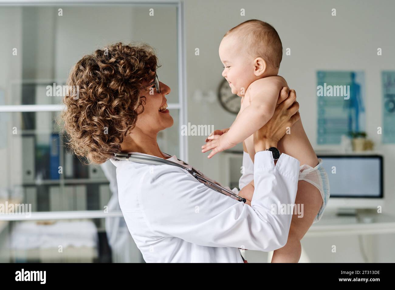 Freundliche Kinderärztin hält Baby auf Armen und lächelt, sie untersucht sie während der medizinischen Untersuchung im Krankenhaus Stockfoto