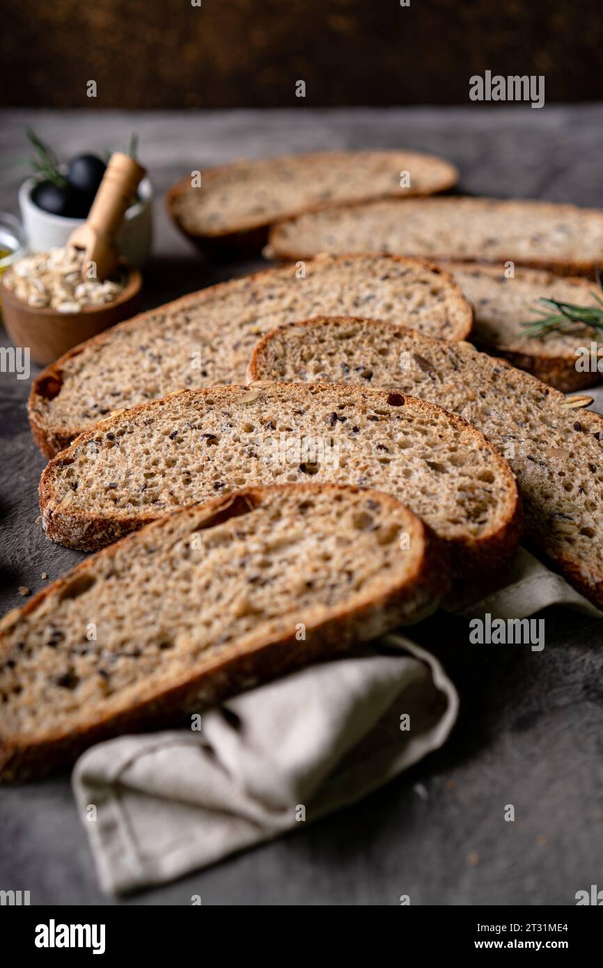 Gebackenes Sauerteigbrot aus Vollkornmehl und Kürbiskernen auf einem Gitter, Olivenöl und schwarze Olive auf einem rustikalen Holztisch. Handwerkliches Brot. Stockfoto