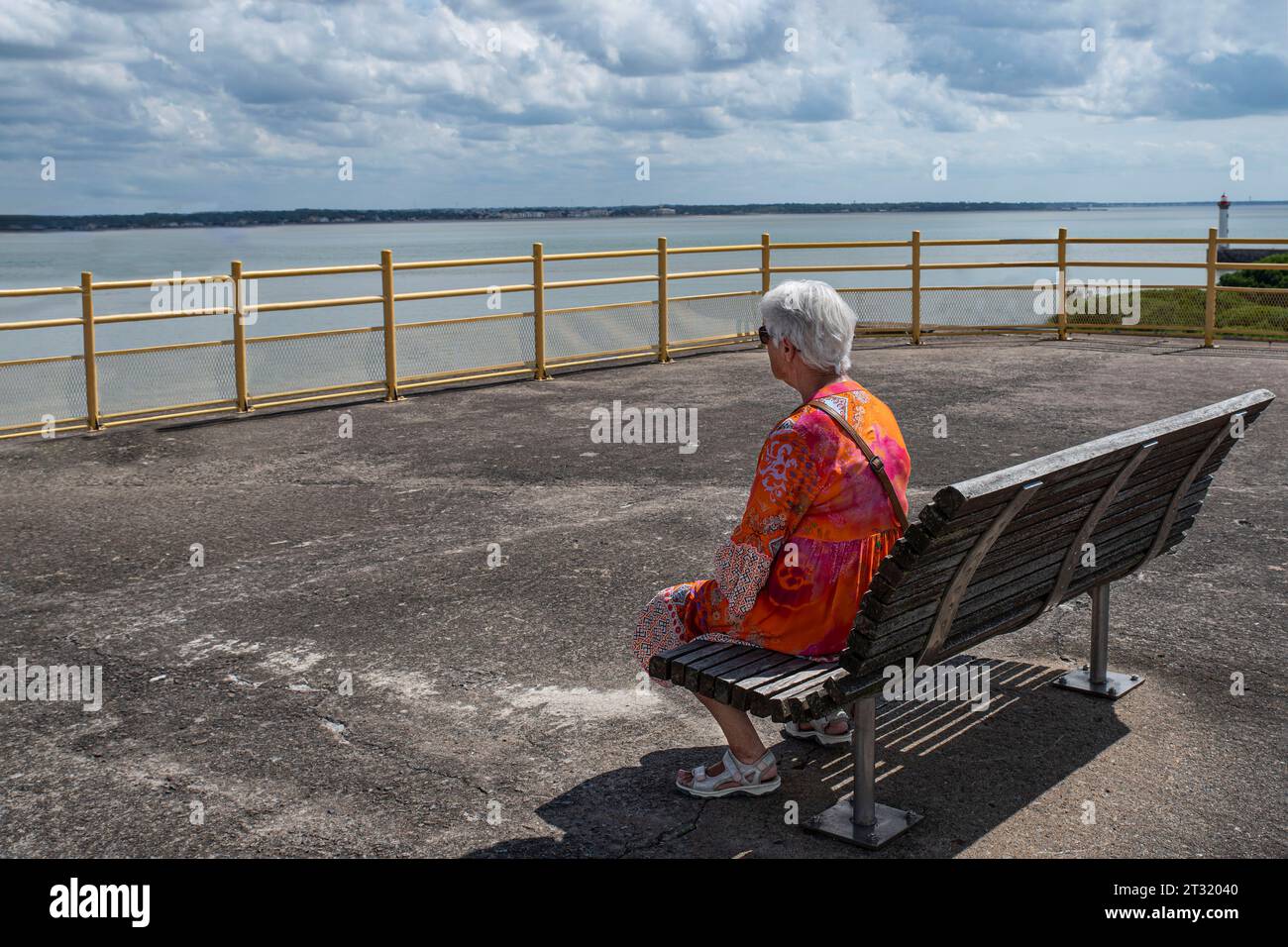 Eine ältere Frau, die auf einer Bank sitzt und auf das Meer blickt Stockfoto