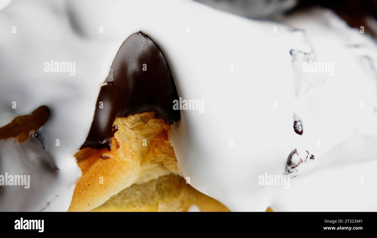 Nachtisch mit Vanillepudding. Stock Clip. Große saftige Schokoladen-Eclairs, die mit Zucker-weißer Sahne gegossen und geschlossen entfernt werden. Stockfoto