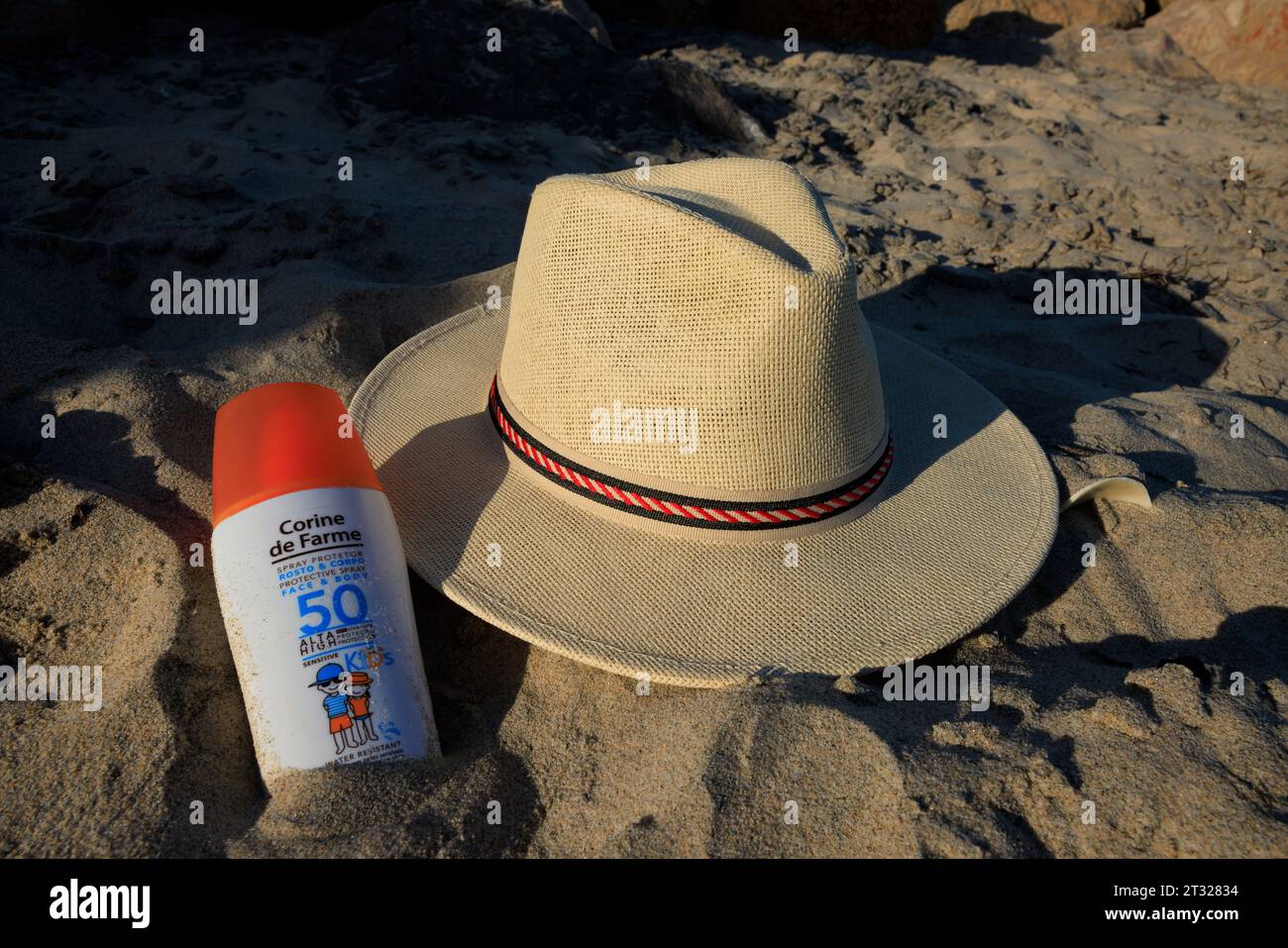 Sonnencreme-Flasche und Panama-Sonnenhut im Sand an einem Strand auf Ilha do Farol (Leuchtturminsel) vor der Küste von Olhão in Portugal. Stockfoto