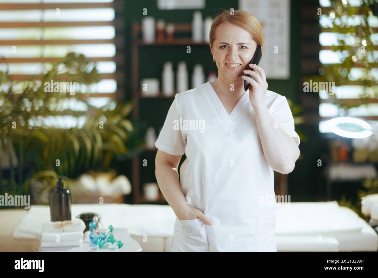 Gesundheitszeit. Lächelnde Massagetherapeutin Frau im Massageschrank, die mit einem Smartphone spricht. Stockfoto