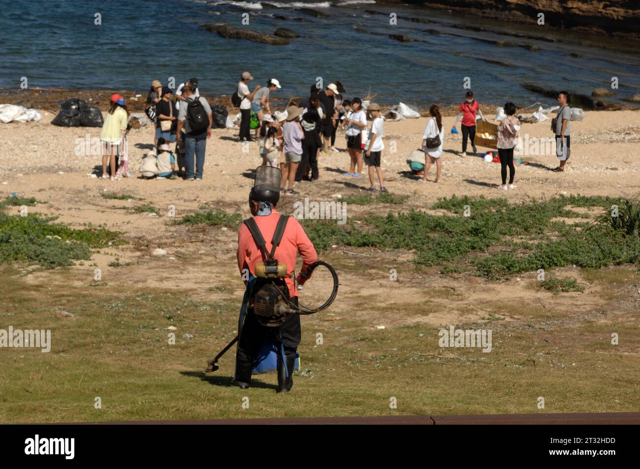 Mann, der mit einem Peitschenschneider Gras schneidet, Yehliu Geopark, New Taipei City, Taiwan. Stockfoto