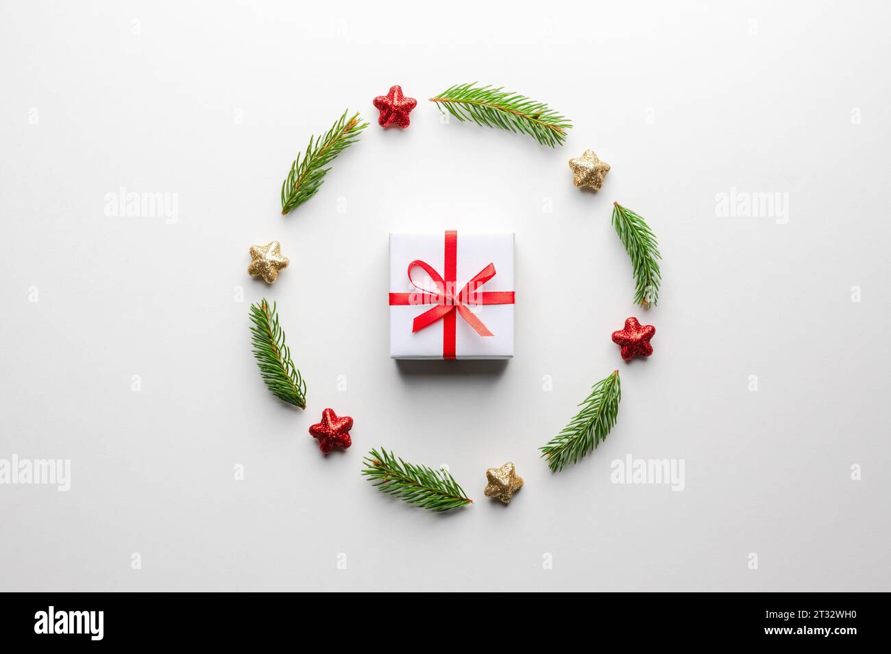 Kreativer Weihnachtshintergrund mit Weihnachtsgeschenkkasten mit rotem Band, Kugeln, Tannenzweigen und goldenen Sternen auf weißem Hintergrund. Flach, Draufsicht, Kopierraum Stockfoto