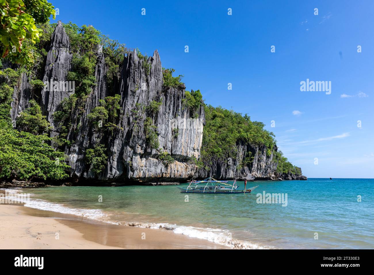 Riesige Karstklippen erheben sich aus dem Wasser über einem tropischen Strand mit dem traditionellen philippinischen banca-Boot, das vor der Küste schwimmt Stockfoto