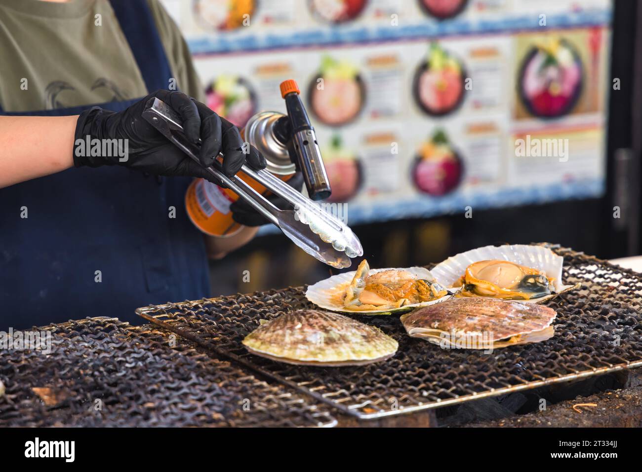 Ein Koch in einer Straßenküche auf dem berühmten Fischmarkt Tsukiji in Tokio, Japan, bereitet Meeresfrüchte mit einem Bunsenbrenner zu Stockfoto