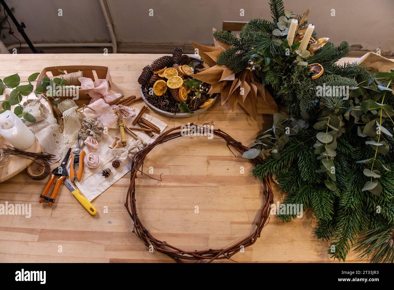 Meisterkurs, Anleitung, DIY, wie man Weihnachtskranz für den Advent macht. Auf Holztisch: Tannenzweige, Eukalyptus, Kranzbasis, Bänder, Schere, Dr Stockfoto