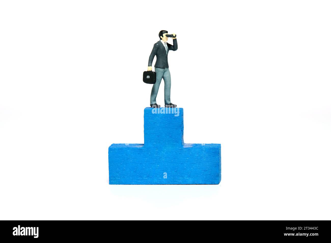 Miniatur-Kleinkinder-Spielfiguren-Fotografie. Illustration des Konzepts der gewinnenden Taktik. Ein Geschäftsmann, der ein binokulares Teleskop benutzt, steht über dem blauen Podium Stockfoto