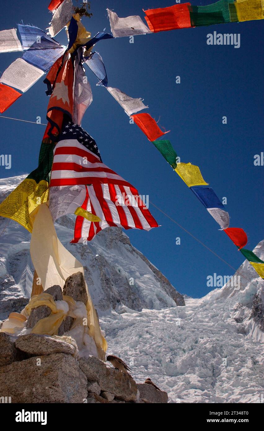 Amerikanische und nepalesische Fahnen mischen sich mit tibetisch-buddhistischen Gebetsfahnen, die über dem Khumbu-Basecamp des Everest flattern. Stockfoto