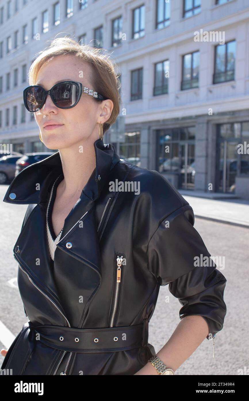 Eine 35-jährige junge Frau in schwarzem Ledermantel und Sonnenbrille Stockfoto