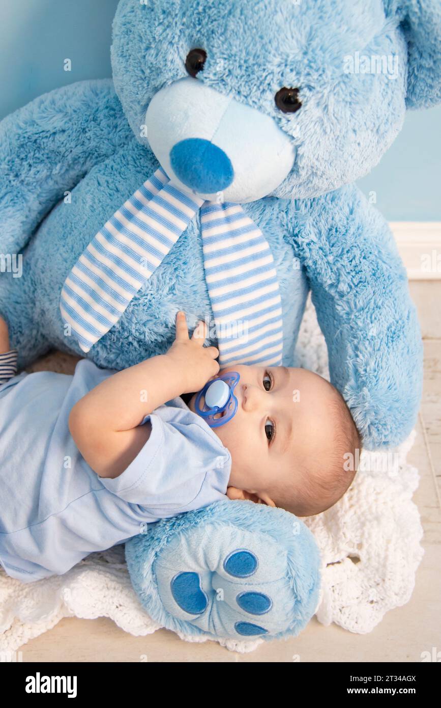 Postkarte eines schönen Babys, das mit einem großen blauen Teddybären spielt Stockfoto
