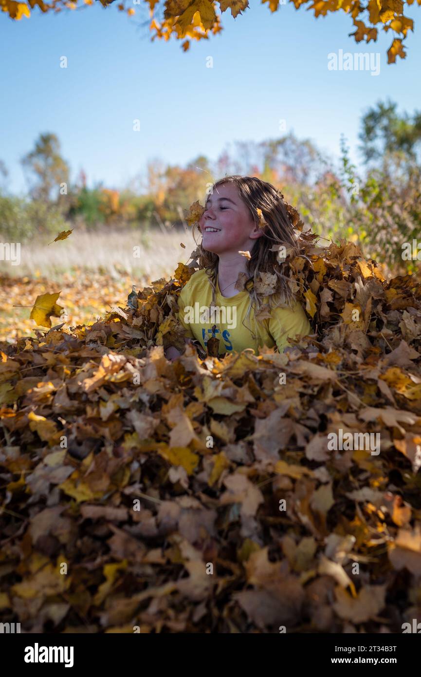 Lächelnd, sitzend in einem Haufen herbstlicher Blätter Stockfoto