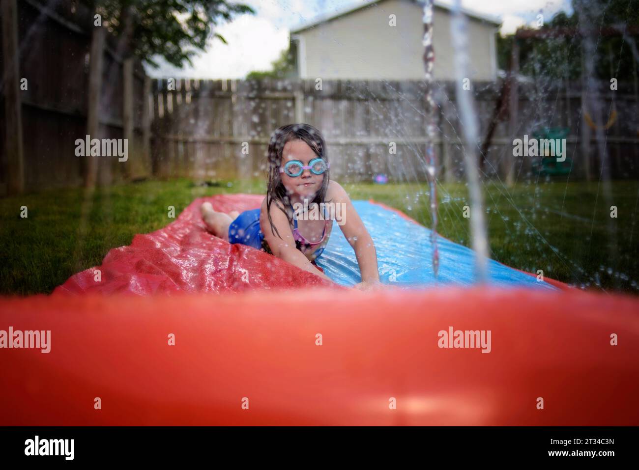 Kleines Mädchen, das mit einer Schutzbrille auf der Wasserrutsche spielt Stockfoto