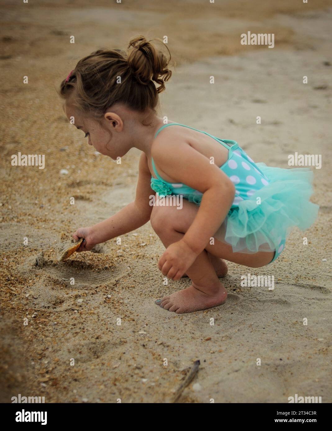 Kleines Mädchen, das in blauem Badeanzug im Sand gräbt Stockfoto