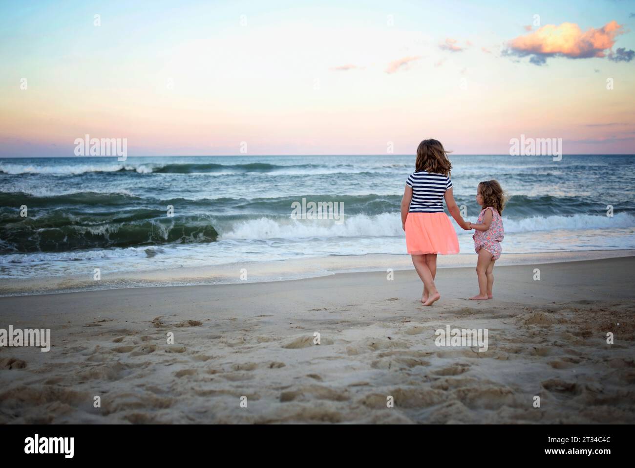 Schwestern, die Hände halten und den Sonnenuntergang auf dem Meer beobachten Stockfoto