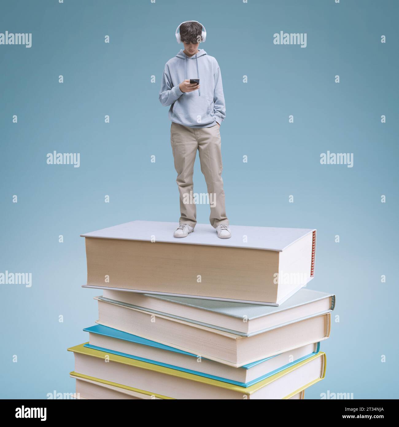 Junge Schülerin mit Smartphone und auf einem Bücherstapel stehend: Online-Lern- und Bildungskonzept Stockfoto