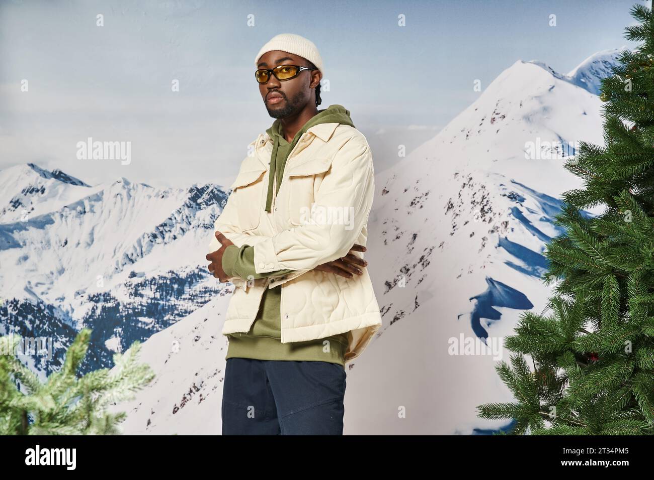 Hübscher afroamerikanischer Mann in weißer Jacke mit überkreuzten Armen, der in die Kamera blickt, Wintermode Stockfoto