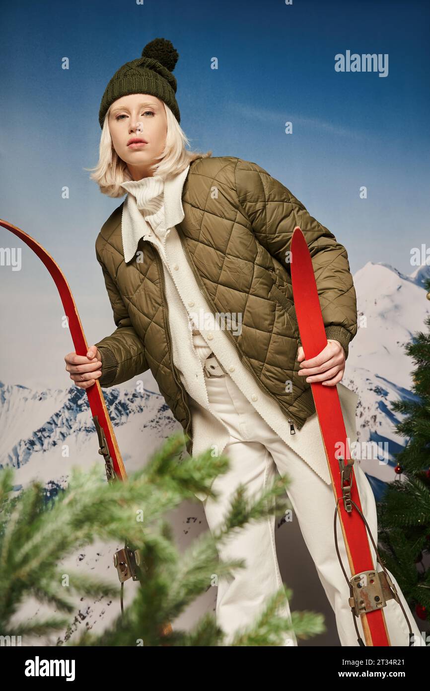 Attraktive junge Frau in warmer Jacke posiert mit Skiern auf schneebedecktem Hintergrund, Winterkonzept Stockfoto