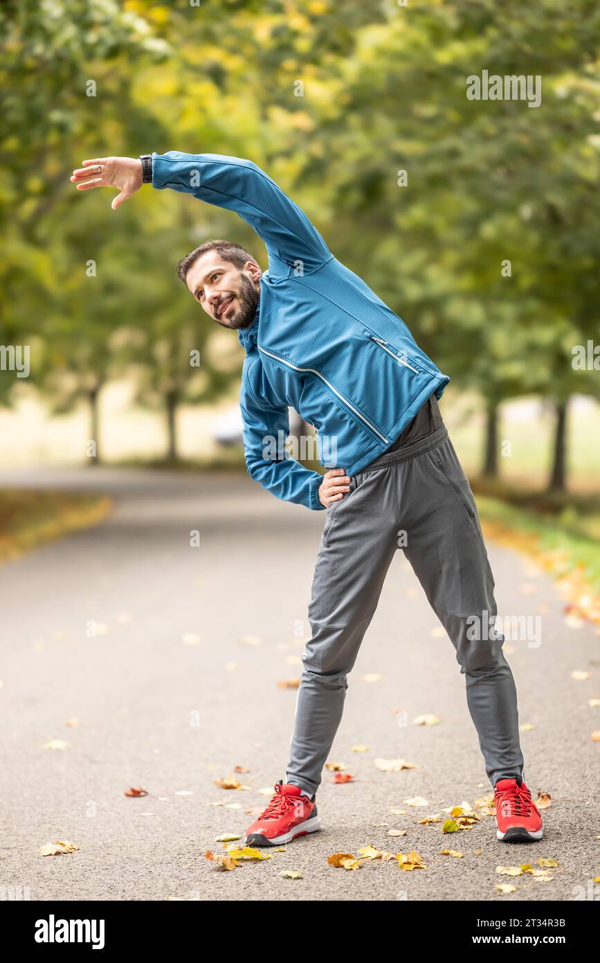 Ein junger Athlet wärmt sich vor dem Lauftraining im Park auf. Sie erwärmt den oberen Teil des Körpers. Stockfoto