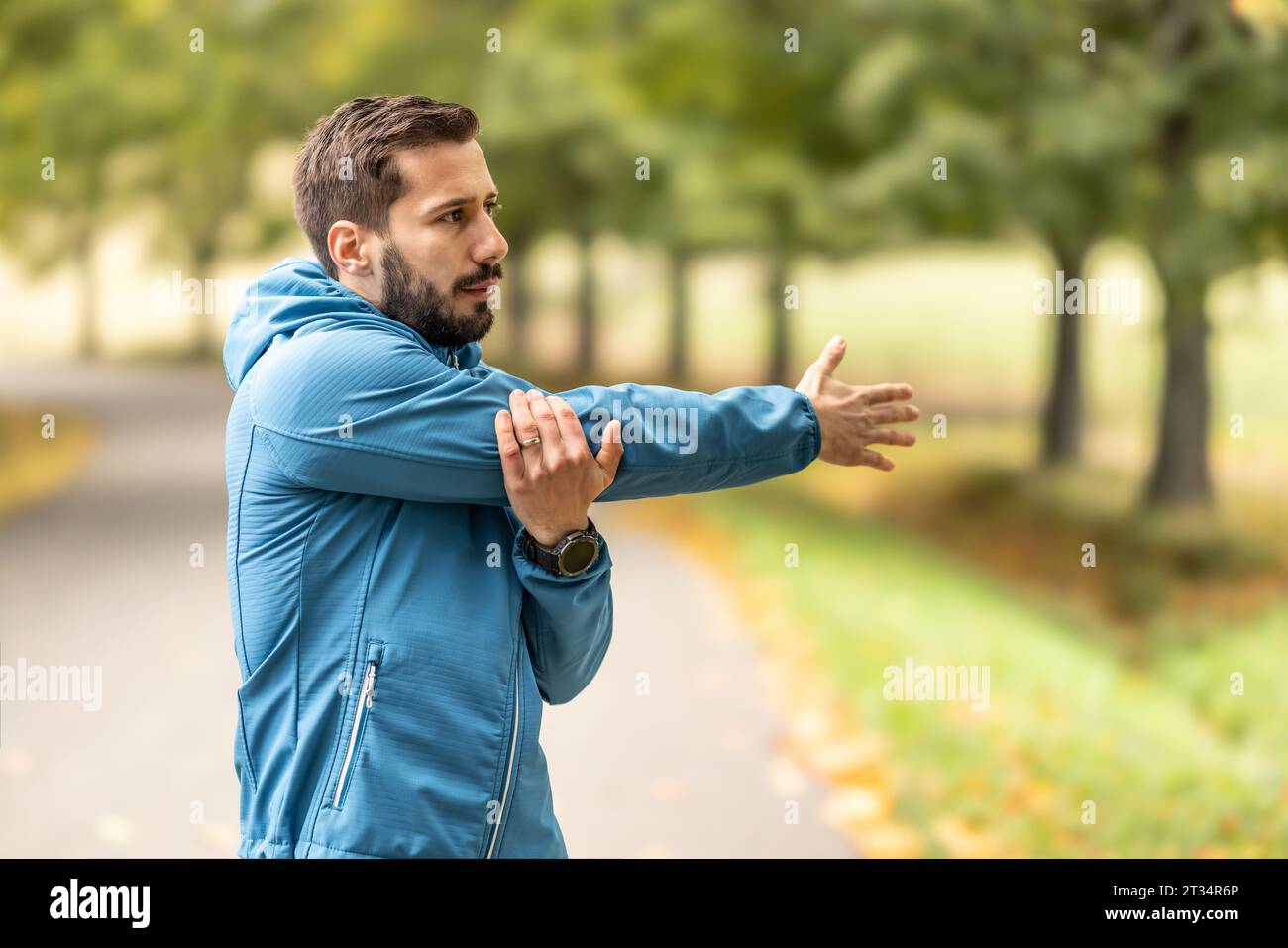 Ein junger Athlet wärmt sich vor dem Lauftraining im Park auf. Sie erwärmt den oberen Teil des Körpers. Stockfoto