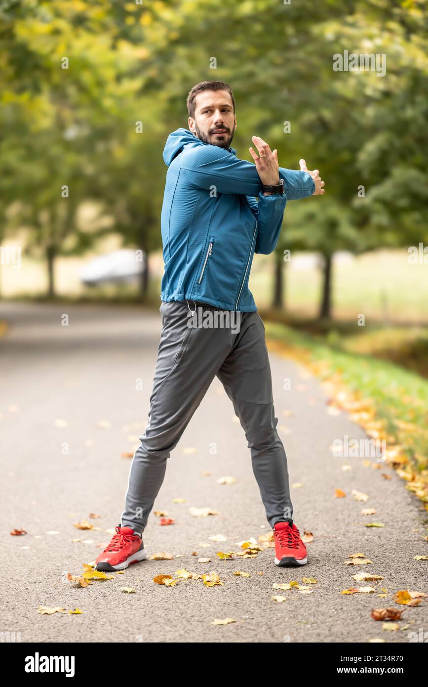 Ein junger Athlet wärmt sich vor dem Lauftraining im Park auf. Sie erwärmt den oberen Teil des Körpers. Stockfoto