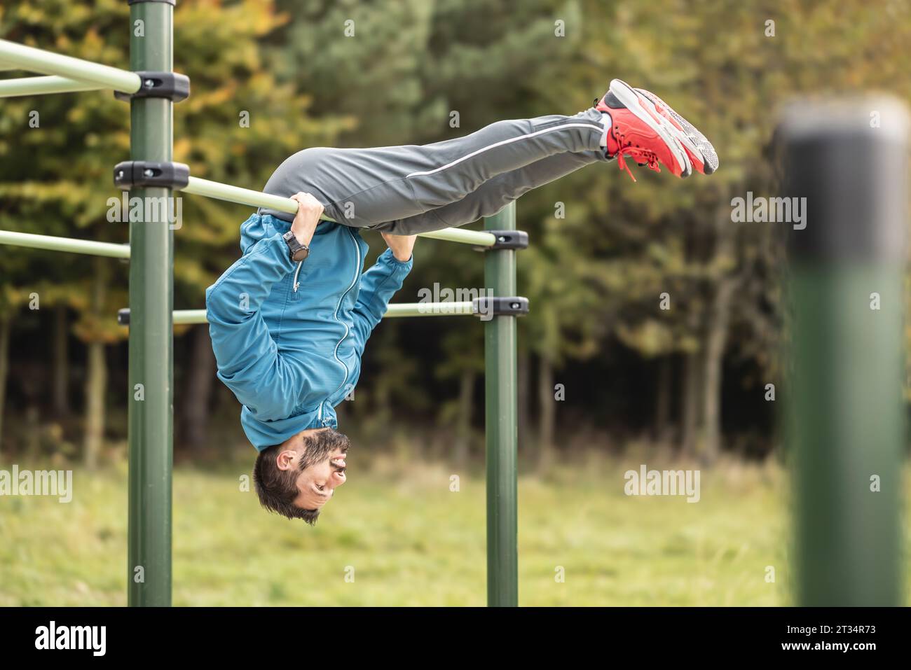 Junger Mann, der Calisthenics in einem Fitnessstudio im Freien mit parallelen Bars ausführt. Ein gut aussehender Athlet macht Gymnastikübungen auf einem Outdoor-Sportfie Stockfoto