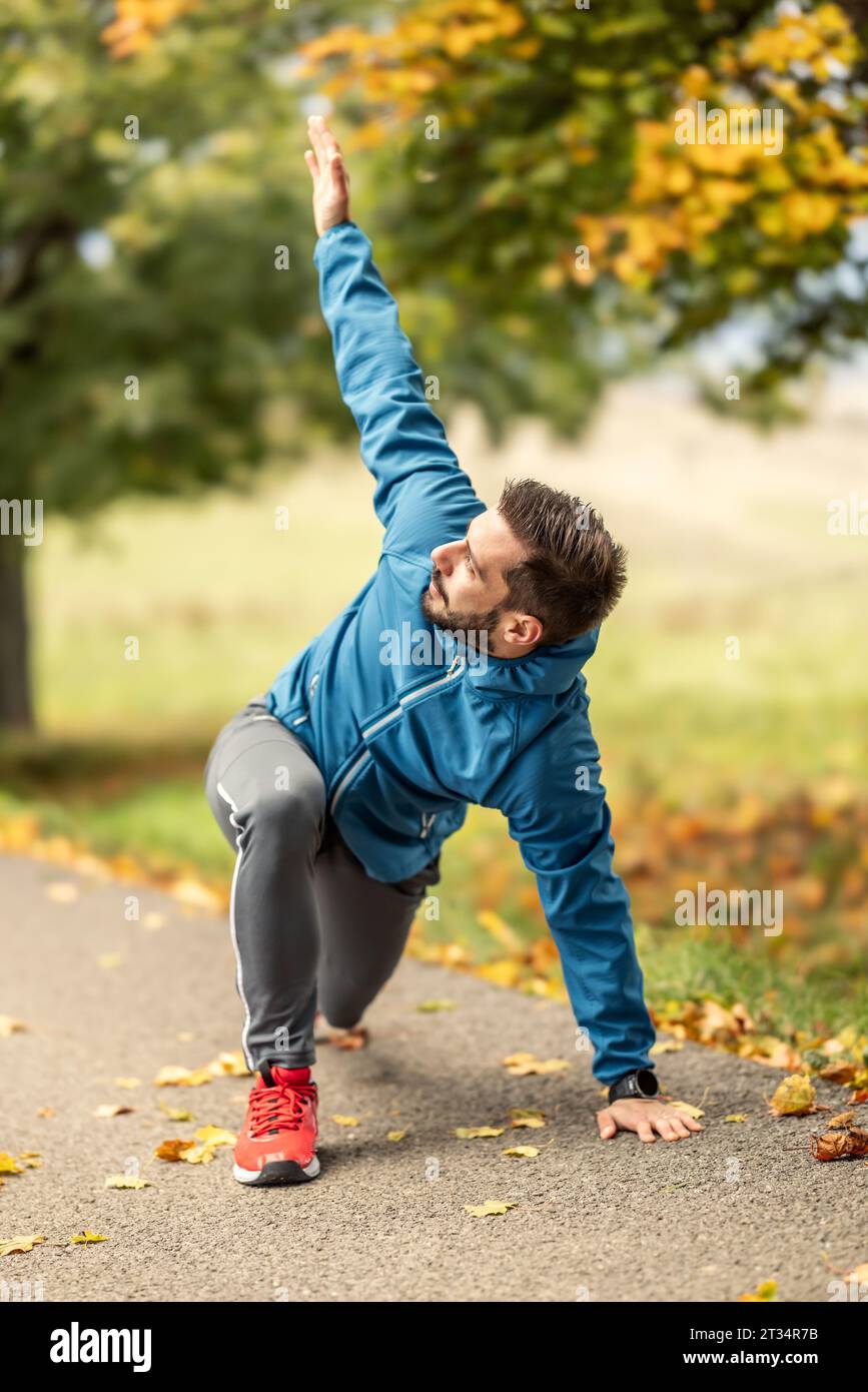 Ein junger Athlet wärmt sich vor dem Lauftraining im Park auf. Sie erwärmt den oberen und unteren Teil des Körpers. Stockfoto